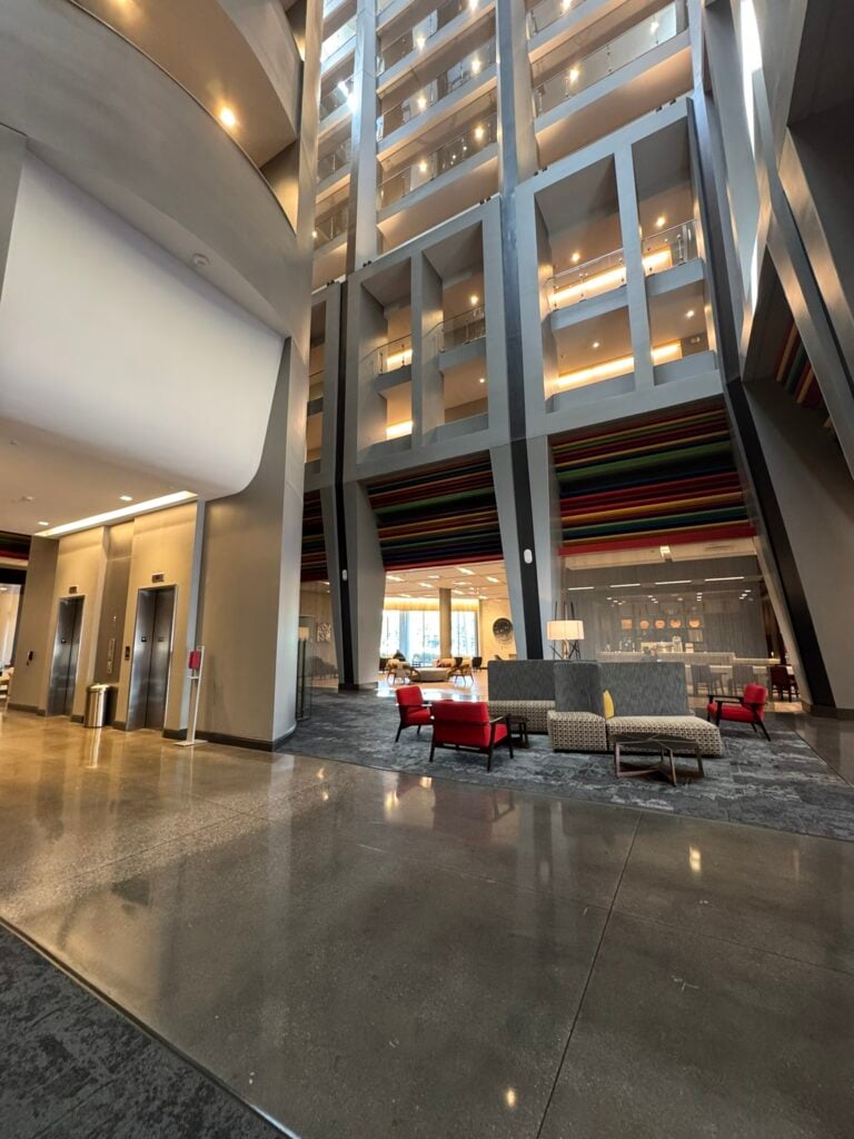 Family-Friendly Hotel in Cincinnati: Our Stay at The Summit Hotel 9 A modern building lobby with polished floors, red and beige seating, high ceilings, and multiple floors visible through large interior windows.