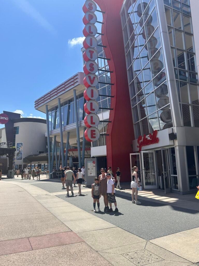 A group of four people stand outside Splitsville, one of the Top 3 Must-Pick Family Friendly Restaurants at Disney Springs, with its red vertical sign shining on a sunny day as other pedestrians pass by.