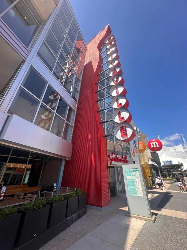 Tall modern building with a red vertical SPAGHETTI sign next to outdoor planters; blue sky and other colorful storefronts in the background—one of the Top 3 Must-Pick Family Friendly Restaurants at Disney Springs.
