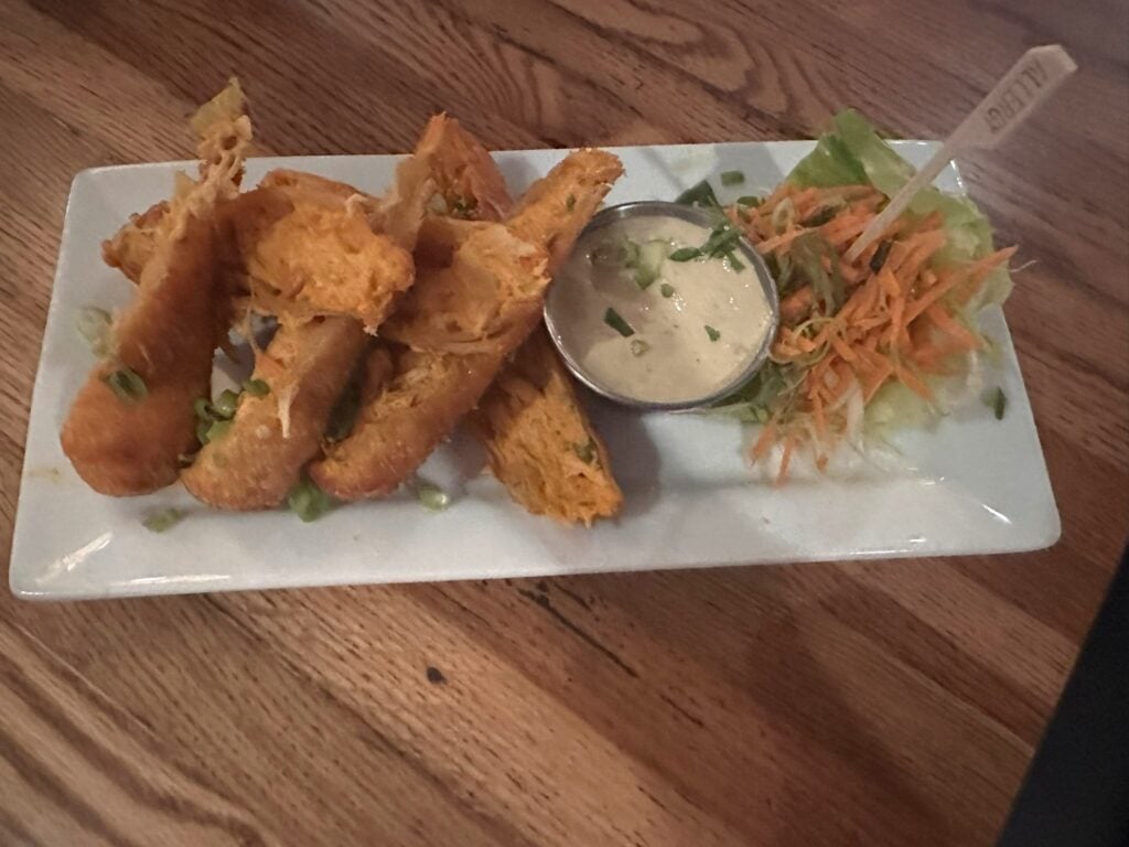 A rectangular plate with several pieces of fried food, a cup of creamy dipping sauce, and a small side of shredded lettuce and carrot salad—just one tasty option at the Top 3 Must-Pick Family Friendly Restaurants at Disney Springs.