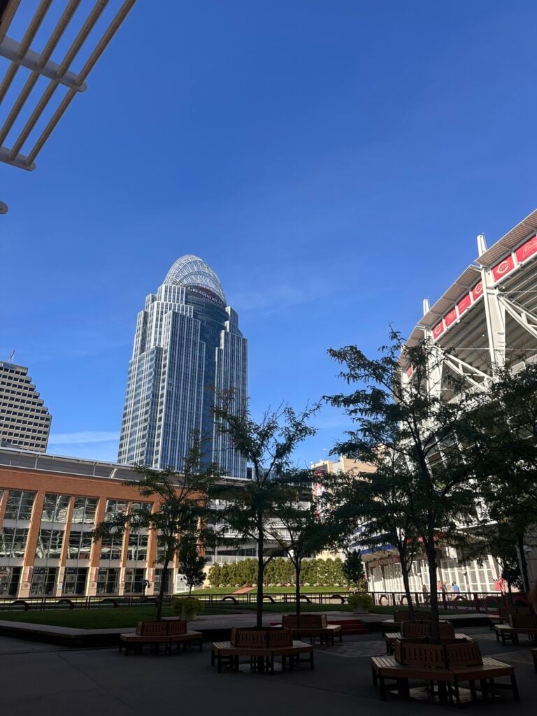 Family-Friendly Hotel in Cincinnati: Our Stay at The Summit Hotel 6 Tall glass office building under a clear blue sky, with trees, benches, and a stadium visible in the foreground.